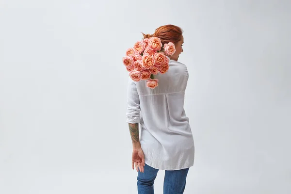 back view of red haired woman holding bouquet of pink roses