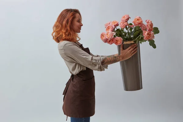 エプロン ピンクのバラの花束花瓶を持って幸せな若い赤髪女 花ショップ コンセプト — ストック写真