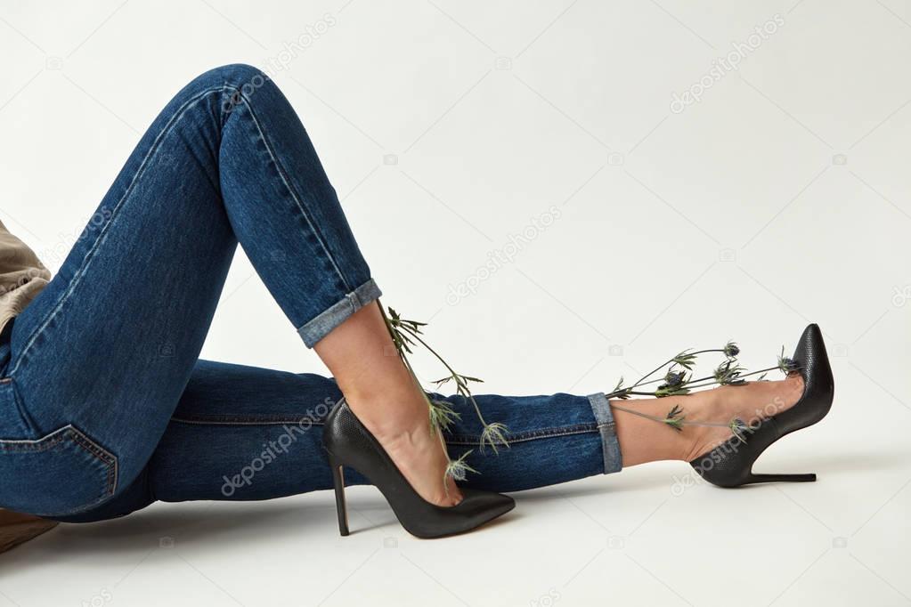 slim beautiful female legs in jeans and black high heel shoes decorated blue eryngium  flowers on a white background, Valentine's Day Concept 