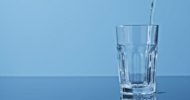 Sauberes Wasser Das Glas Auf Blauem Hintergrund Gegossen Wird — Stockvideo