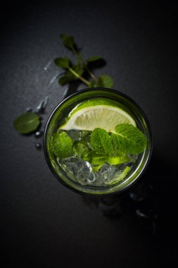 Buzlu Mojito kokteyl bardak ve malzemeler, kireç, buz ve nane yaprakları siyah arka plan üzerine, soğuk yaz içeceği 