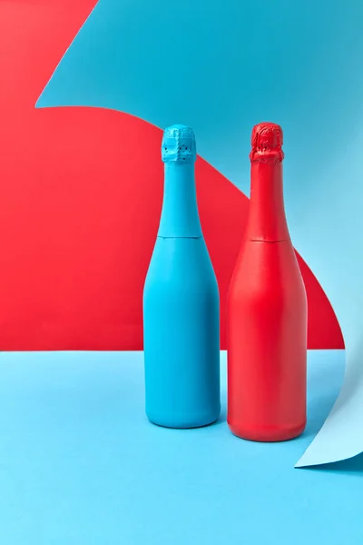两只富有创意的葡萄酒造型瓶 在双色波浪形背景上喷上了红色和蓝色的喷雾 并附有文字 — 图库照片