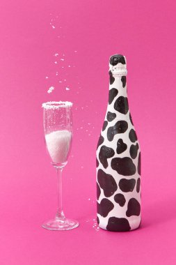 Siyah lekeli dekoratif beyaz şarap şişesi ve pembe arka planda düşen beyaz tozlu cam, mesaj için yer. Tebrik kartı..