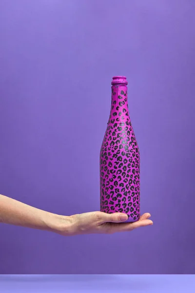 香槟酒瓶在一个女人手上的紫丁香背景上涂上了炽热的粉色和黑色斑点 复制空间 平躺在床上 假日概念 — 图库照片