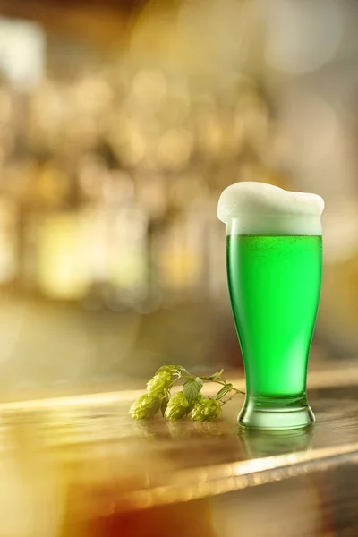 冷たい緑のビールと緑のホップの枝のガラスは あなたのテキストのための無料のスペースを持つパブで木製のバーカウンターで ハッピー セント パトリックの日のコンセプト — ストック写真