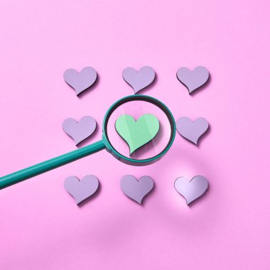 Big loupe, diğer lavanta renkli kalplerin etrafındaki yeşil kalbin boyunu arttırıyor. Pastel pembe arka plan, kopyalama alanı. Sevgililer Günü tebrik kartı..