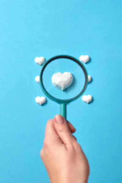 女人的手拿着大大的放大镜 上面有聚精会神的石膏状的心形图案 背景是淡蓝色的 复制空间 情人节贺卡 — 图库照片