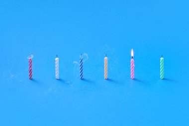 Renkli üflenmiş mumların doğum günü kartı. Bir tanesi mavi arka planda yanıyor. Kopya alanı. Doğum günü partisi kartı kompozisyonu