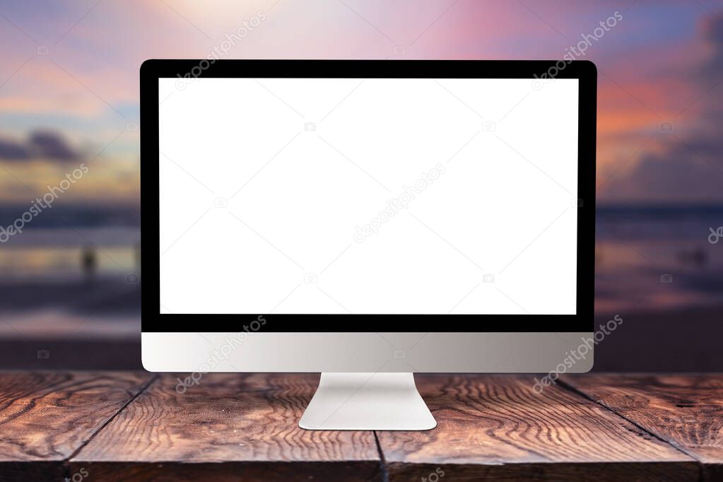 Empty white mock-up computer display on a wooden table against blurred sea sunset background with bokeh, copy space. Working remotely concept.