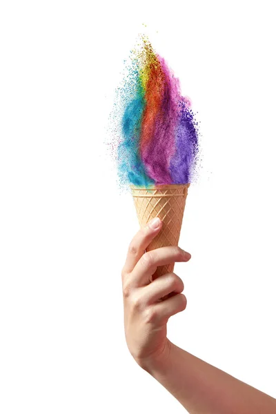 女性の手は 薄い灰色の背景に対してカラフルな虹の塵スプラッシュの形でアイスクリームとワッフルコーンを保持しています コピースペース — ストック写真