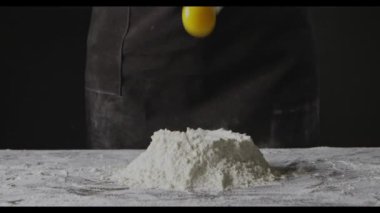 Kadın un içinde yumurta kırıyor, hamur yoğurmaya hazırlanıyor.