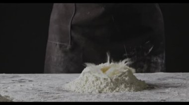 Kadın un içinde yumurta kırıyor, hamur yoğurmaya hazırlanıyor.