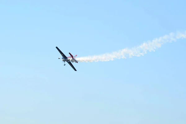 The small smoking plane flies in the sky.