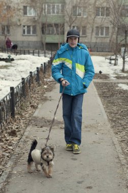 Genç çocuk ceket ile küçük bir köpeği stree üzerinde yürür.