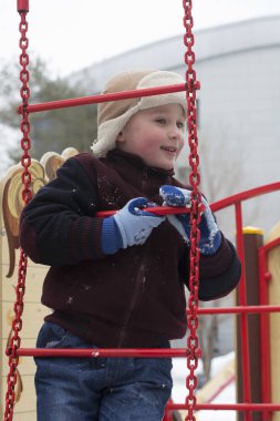 Mutlu küçük çocuk kışın oyun alanında oynuyor.