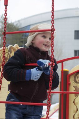 Mutlu küçük çocuk kışın oyun alanında oynuyor.