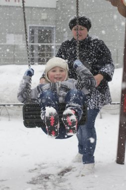 Kar yağışı kışın bir salıncak üzerinde mutlu küçük çocuk sallar