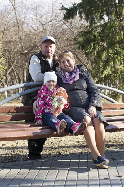 Feliz pareja de ancianos con la nieta sentarse en un banco en th —  Fotos de Stock