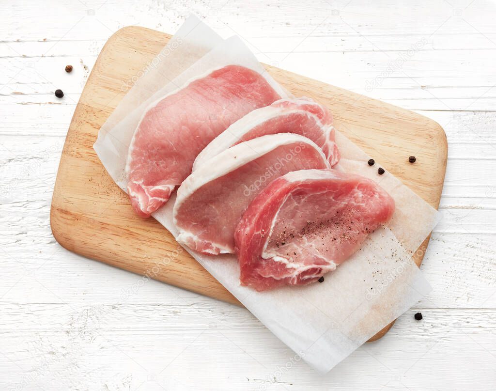 slices of raw pork meat on wooden cutting board, top view