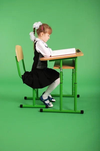 Mädchen in Schuluniform sitzt am Schreibtisch und liest ein Buch — Stockfoto