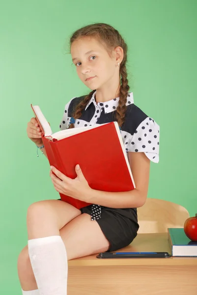 Mädchen in Schuluniform sitzt am Schreibtisch und liest ein Buch — Stockfoto