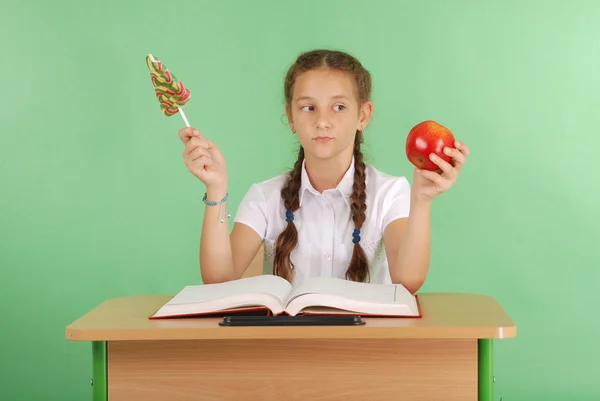 Menina em um uniforme escolar sentado na mesa e escolher doces ou uma maçã — Fotografia de Stock