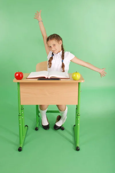 Meisje in een schooluniform zitten aan een bureau en rek — Stockfoto