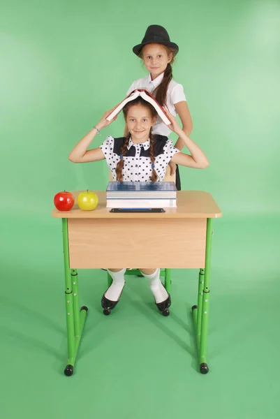 Dos chicas en uniforme escolar sentadas en un escritorio y leyendo un libro —  Fotos de Stock