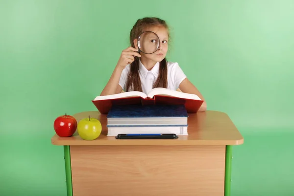 Mädchen in Schuluniform sitzt an einem Schreibtisch mit einer Lupe — Stockfoto