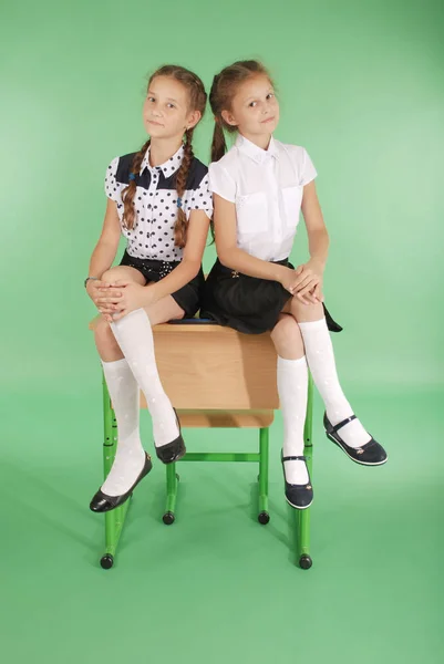 Two girls in a school uniform sitting on desk — Stock Photo, Image