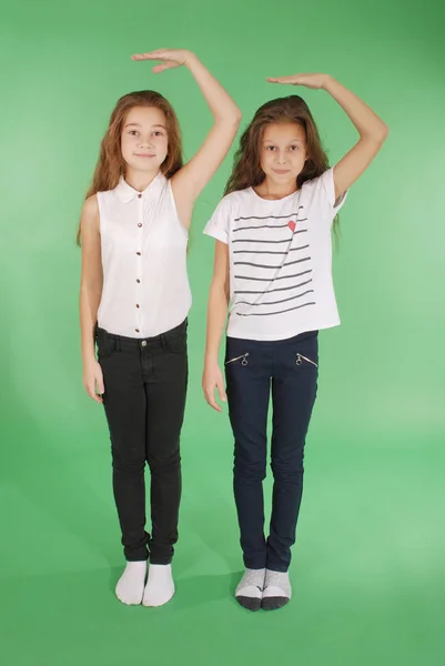 Dos niñas de la escuela toman las manos por encima de la cabeza y miden su crecimiento —  Fotos de Stock