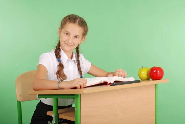 Menina em um uniforme escolar sentado em uma mesa e lendo um livro — Fotografia de Stock
