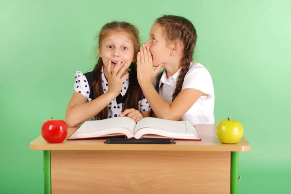 Две школьницы делятся секретами, сидя за столом из книги — стоковое фото