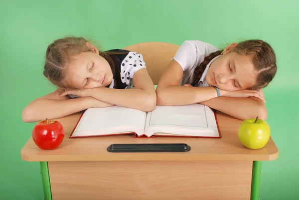 Две школьницы, спящие на стопке книг за ее столом — стоковое фото