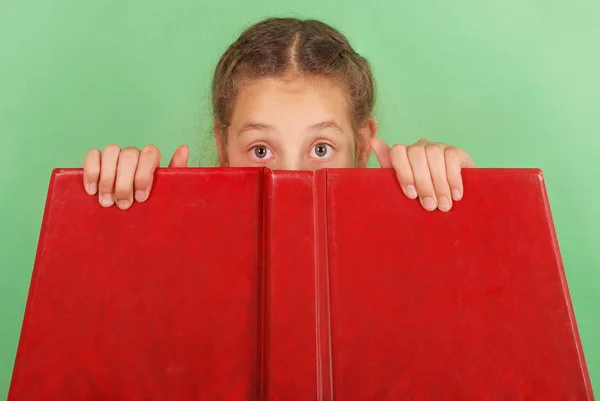 Schönes Schulmädchen, das hinter ihrem roten Buch hervorlugt — Stockfoto