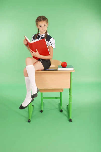 Девушка в школьной форме сидит на столе и читает книгу — стоковое фото