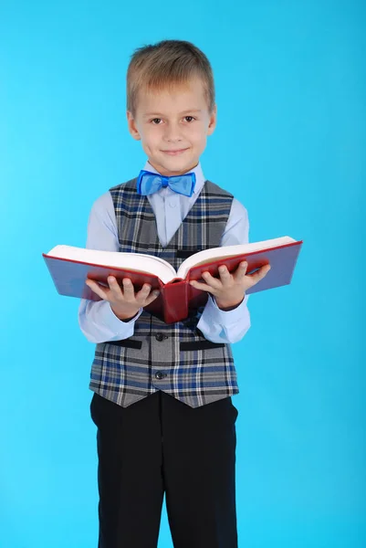 Menino de uniforme escolar segurando um livro vermelho aberto — Fotografia de Stock