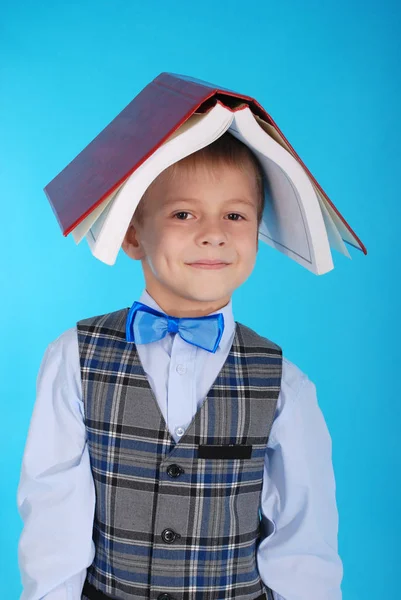 Menino de uniforme escolar segurando um livro na cabeça dela — Fotografia de Stock