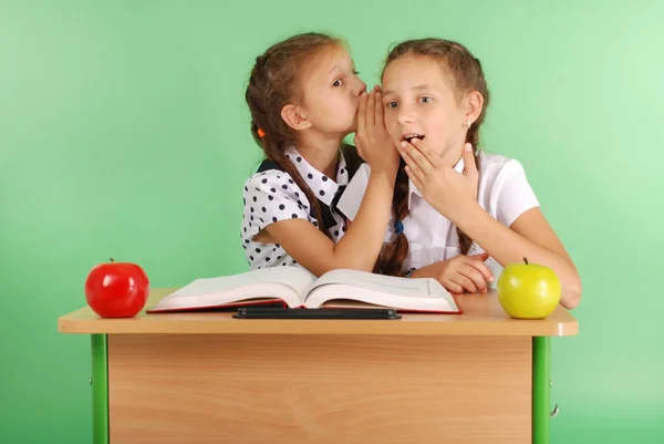 Две школьницы делятся секретами, сидя за столом из книги — стоковое фото