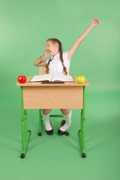 Ragazza in uniforme scolastica seduta a una scrivania e sbadiglia — Foto Stock