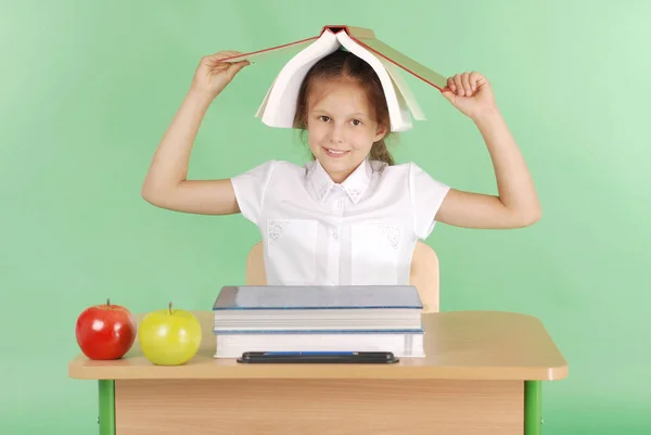 Educación, personas, niños y concepto escolar: niña sentada en un escritorio con un libro en la cabeza —  Fotos de Stock