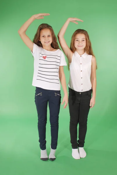 Dos niñas de la escuela toman las manos por encima de la cabeza y miden su crecimiento — Foto de Stock