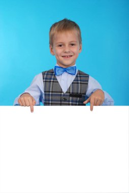 Beyaz bir reklam panosunun arkasına poz gülümseyen bir okul çocuğu