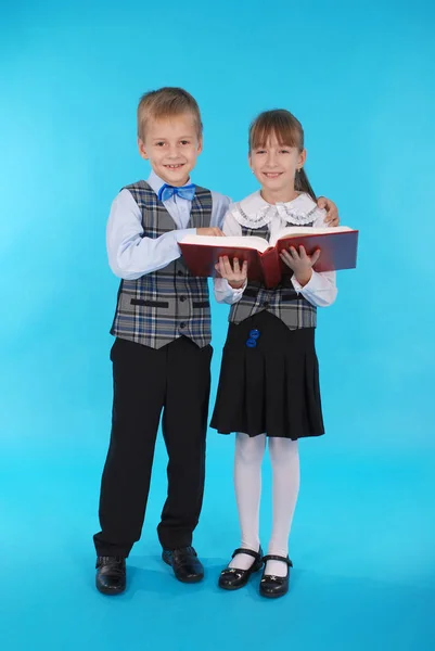 Menino e menina de uniforme escolar lendo um livro — Fotografia de Stock