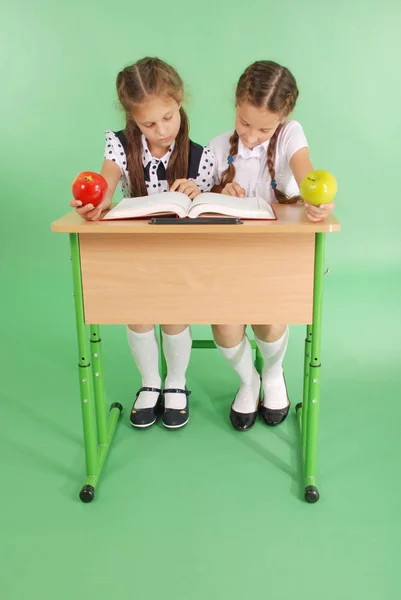 Dos chicas en uniforme escolar sentadas en un escritorio y leyendo un libro —  Fotos de Stock