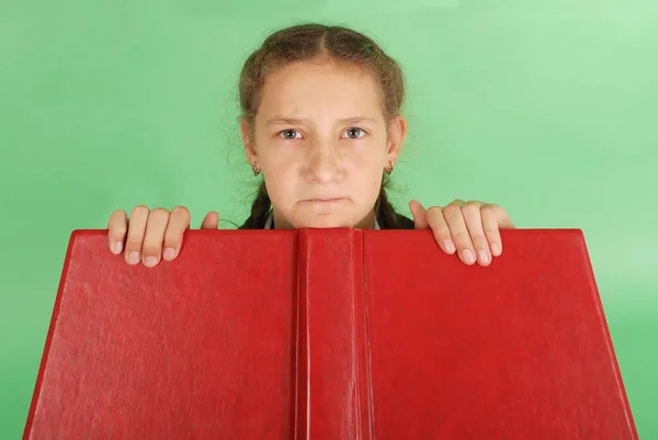 Krásná školačka vykukující zpod její Červená kniha. Vytáhněte obličej — Stock fotografie