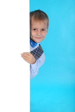 Beyaz bir reklam panosunun arkasına poz gülümseyen bir okul çocuğu