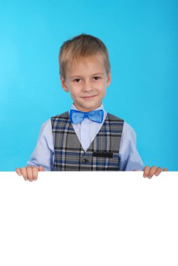 Beyaz bir reklam panosunun arkasına poz gülümseyen bir okul çocuğu