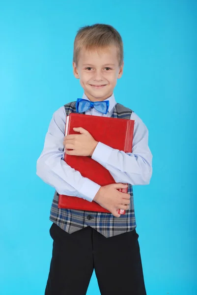 Menino de uniforme escolar segurando um livro vermelho — Fotografia de Stock