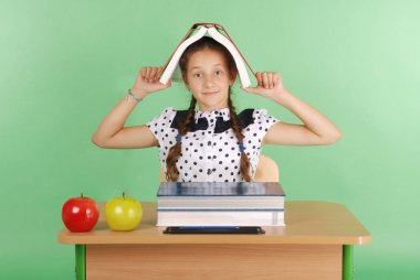 Eğitim, insanlar, çocuklar ve okul kavramı - başında bir kitapla bir masada oturan genç liseli kız